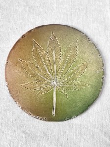 Handmade glazed ceramic trivet with hemp leaf imprint.
